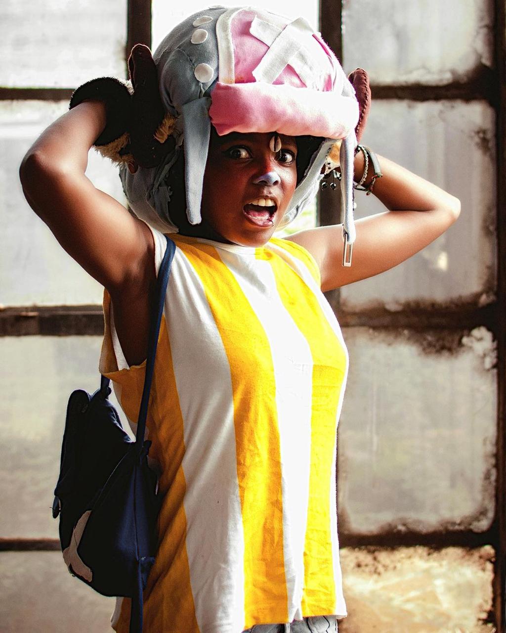 A cosplayer dressed as Tony Tony Chopper from One Piece, adjusting a large plush hat with an expressive face.