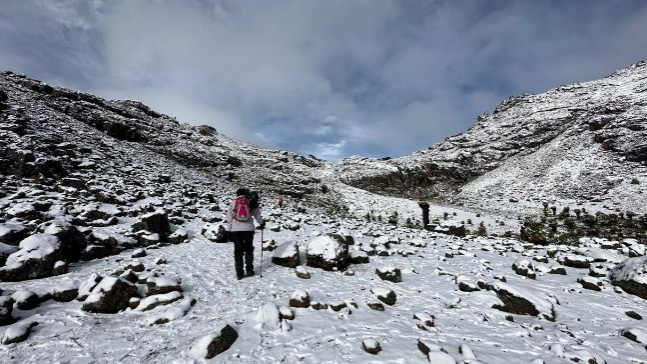 A group of hikers walking through a snowy valley under a brightened sky on Mount Kenya.