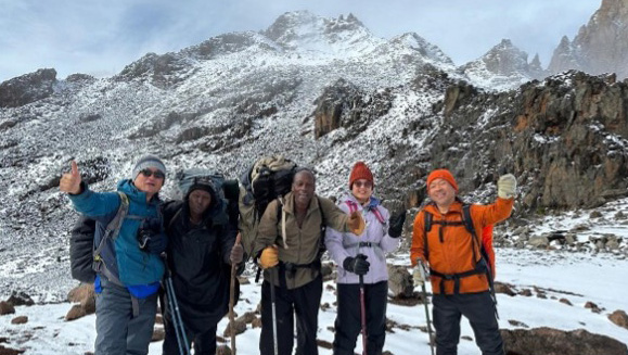 A team of climbers celebrating with thumbs-up gestures near the snowy peaks of Mount Kenya.