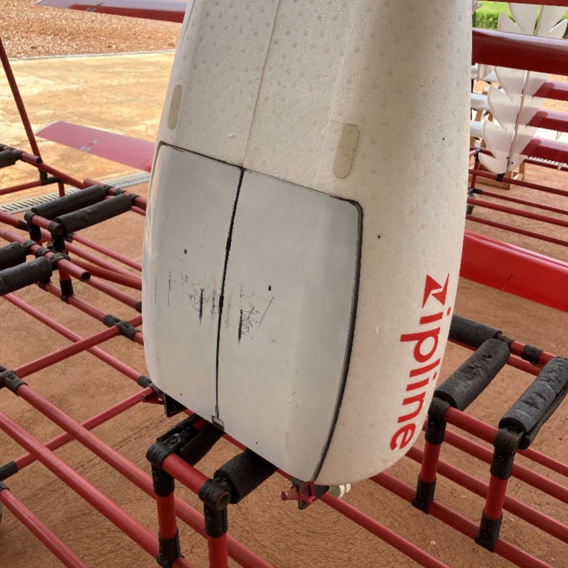 Close-up of the underside of a Zipline medical delivery drone, showing landing wear marks and branding on the tail section.