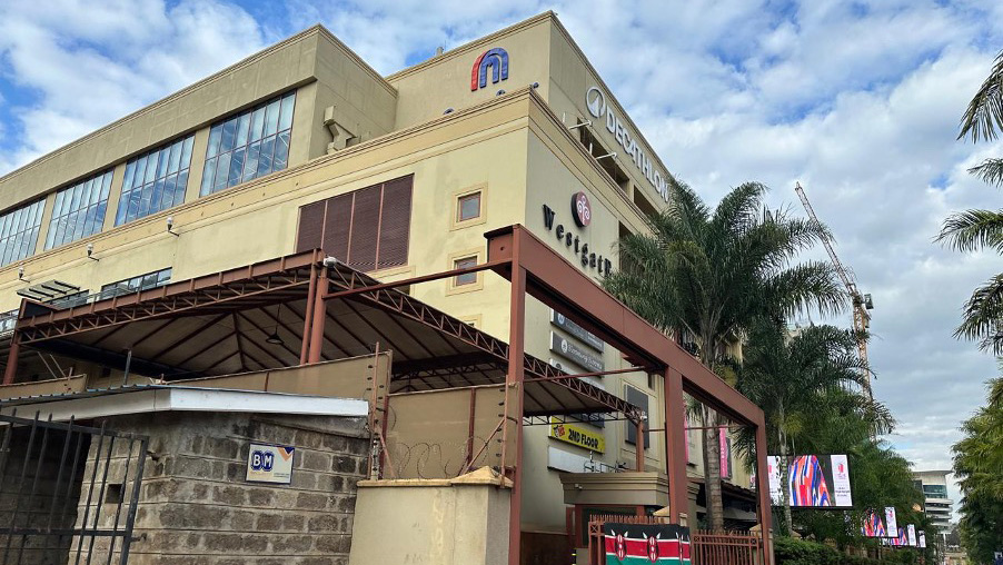 Exterior view of Westgate Shopping Mall in Nairobi, with palm trees and the Kenyan flag at the entrance.