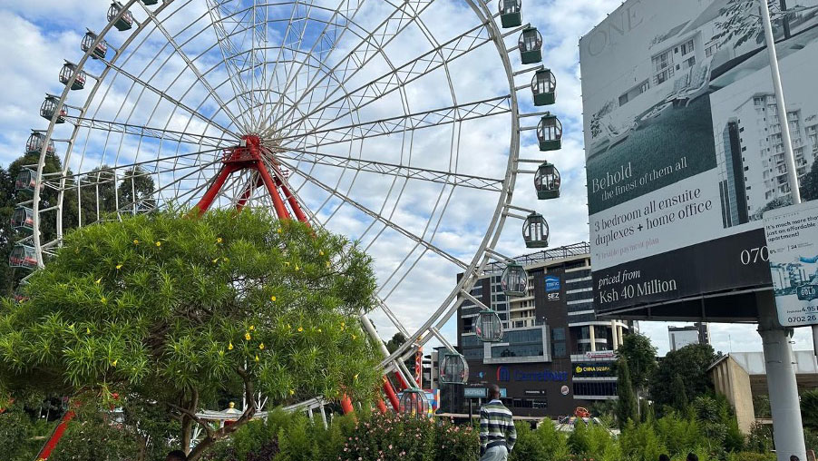 Large Ferris wheel at Two Rivers Mall in Nairobi, with people relaxing on the grassy area in front.