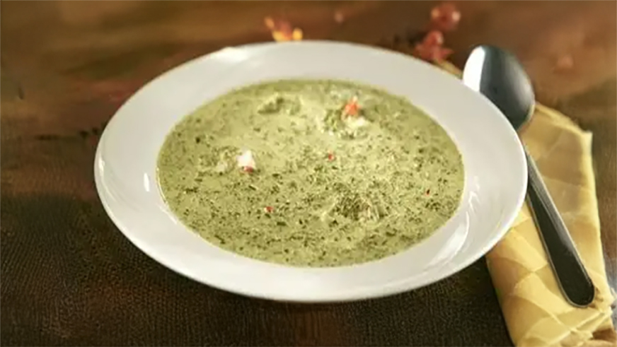 A white bowl of traditional Mozambican green soup made with leafy vegetables and coconut milk.