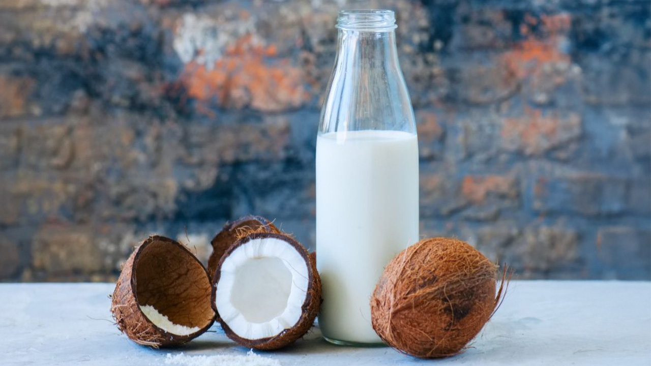 A hand holding a sandwich filled with fried fish cakes, sitting near the beach.