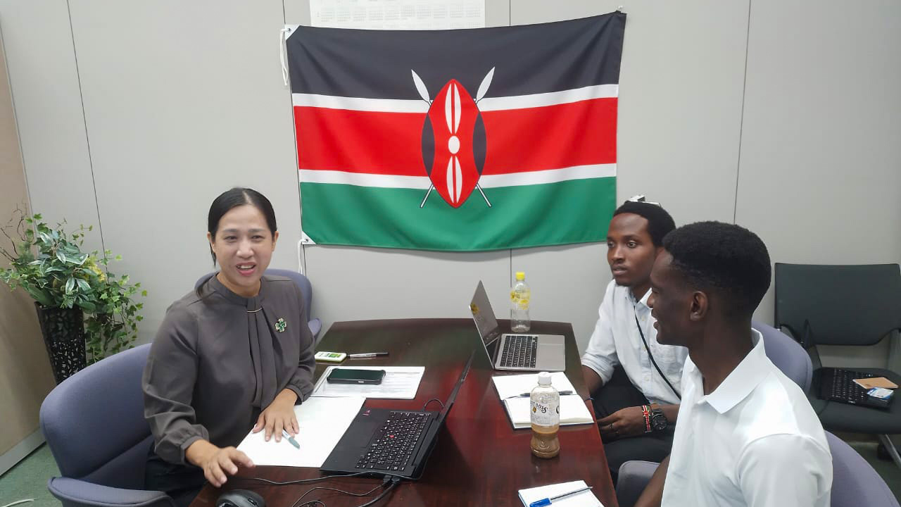 Training session on Japanese business culture, with Baraka and Luwate listening attentively to the instructor under a Kenyan flag.