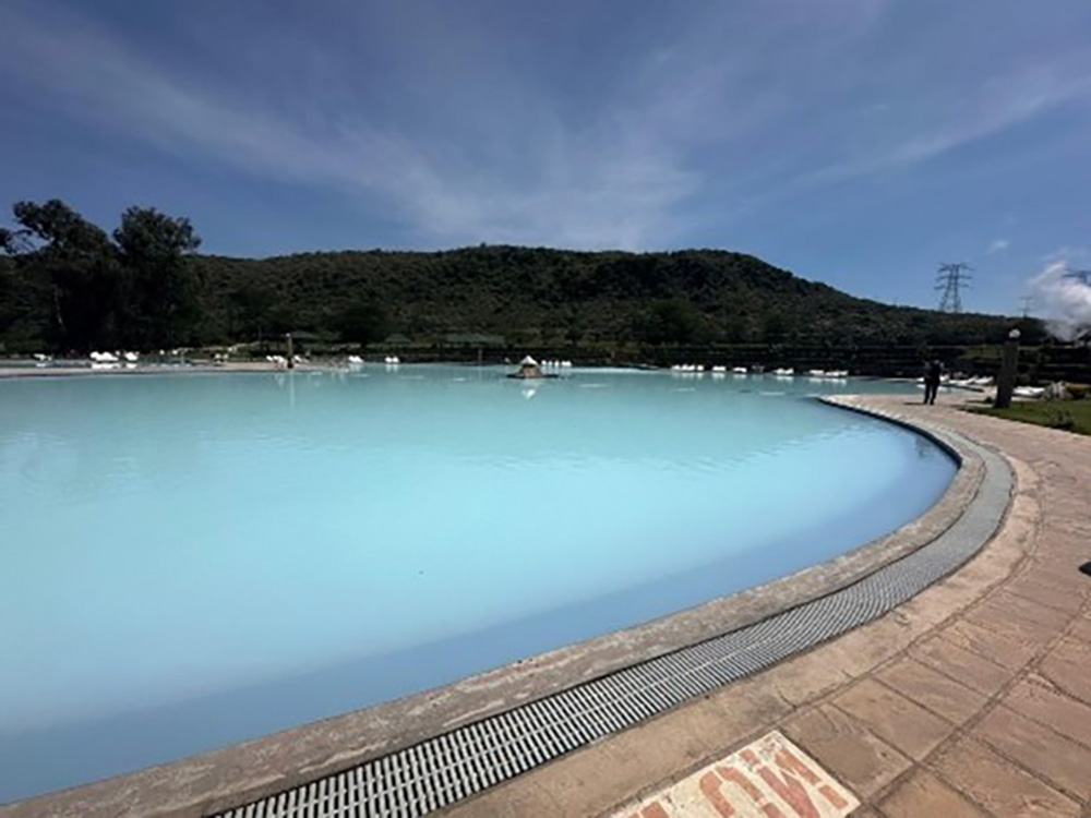 View of the Mvuke Geothermal Spa near Lake Naivasha, Kenya. The spa’s milky blue hot spring water contrasts with the surrounding hills under a bright sky.
