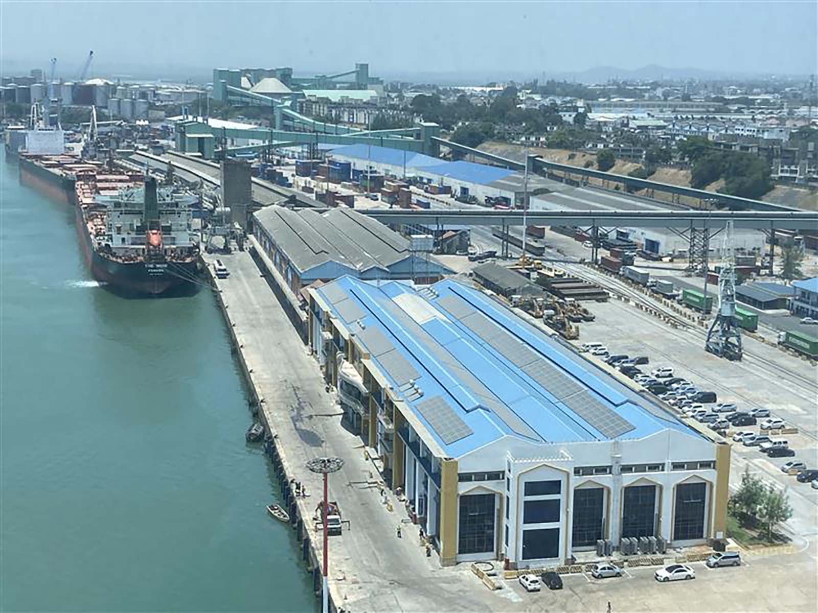 Aerial view of Mombasa Port’s industrial area showing docked cargo ships, warehouses with blue roofs, pipelines, and transport infrastructure extending inland toward the city.