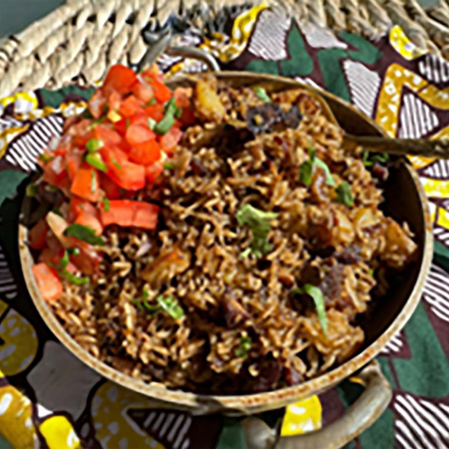 A bowl of Kenyan pilau rice garnished with chopped tomatoes and herbs, placed on patterned fabric.