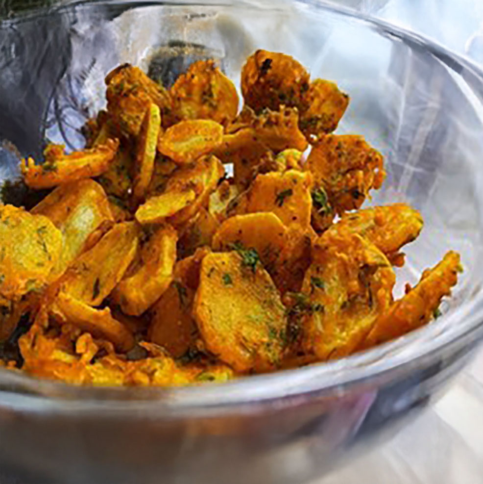 A glass bowl filled with deep-fried, spiced potato slices coated in orange seasoning.