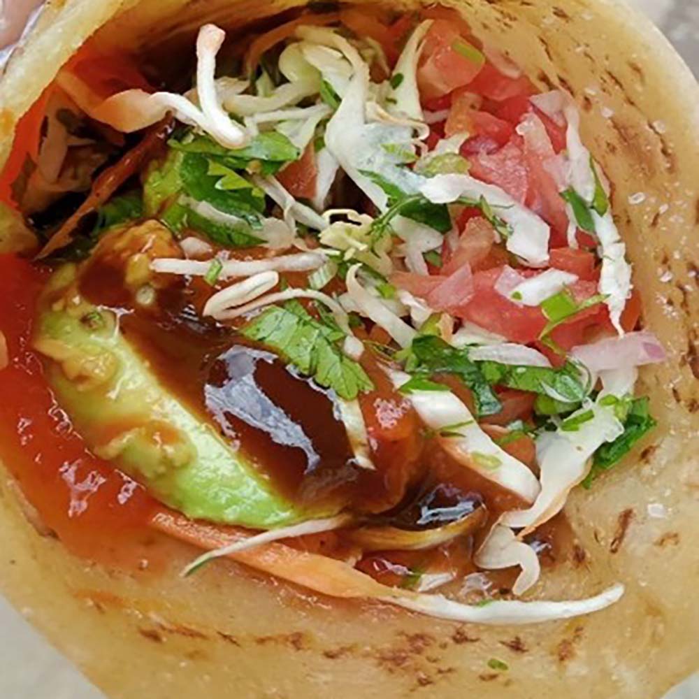 A close-up view of a stuffed chapati wrap filled with avocado, kachumbari, and dark sauce.
