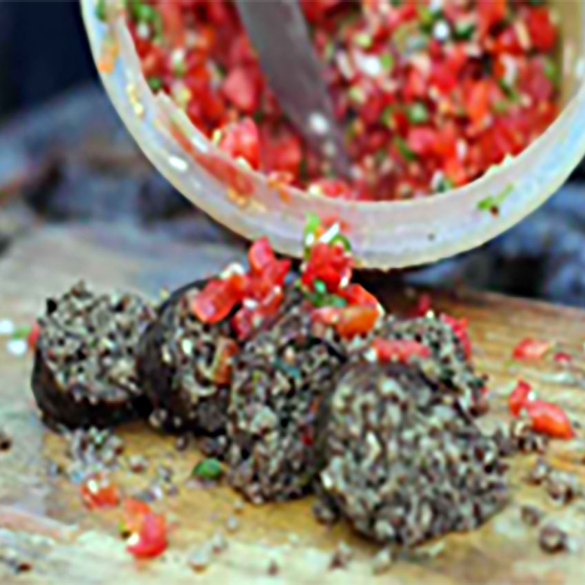 Slices of mutura sausage on a wooden board topped with diced tomatoes and onions.