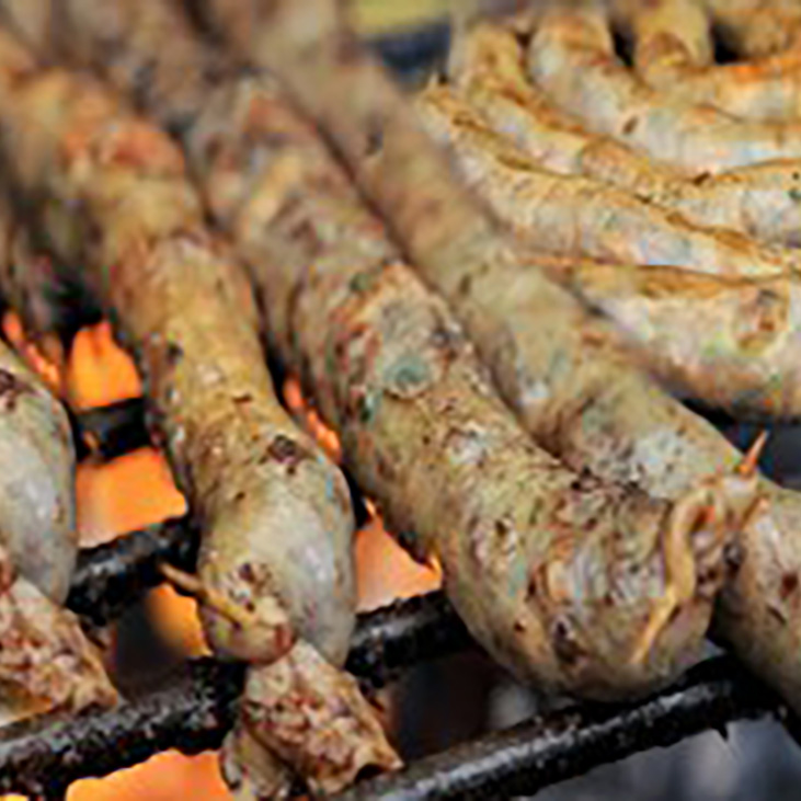 Mutura sausages grilling over open flames on a metal grate.