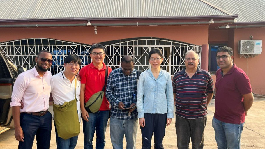 A group photo of team members standing together outside a building in Ghana during the site visit, smiling and posing for the camera.