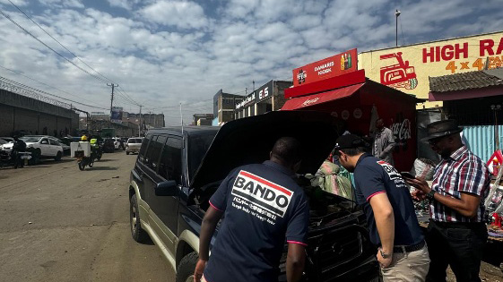 Bando Chemical staff inspecting a vehicle with local mechanics at a roadside automotive repair shop in Nairobi.