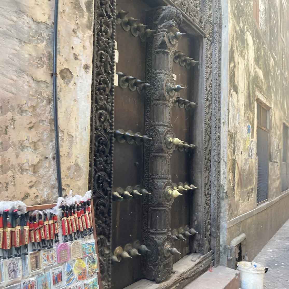 Traditional Zanzibar wooden door with ornate carvings and metal studs along a Stone Town street.