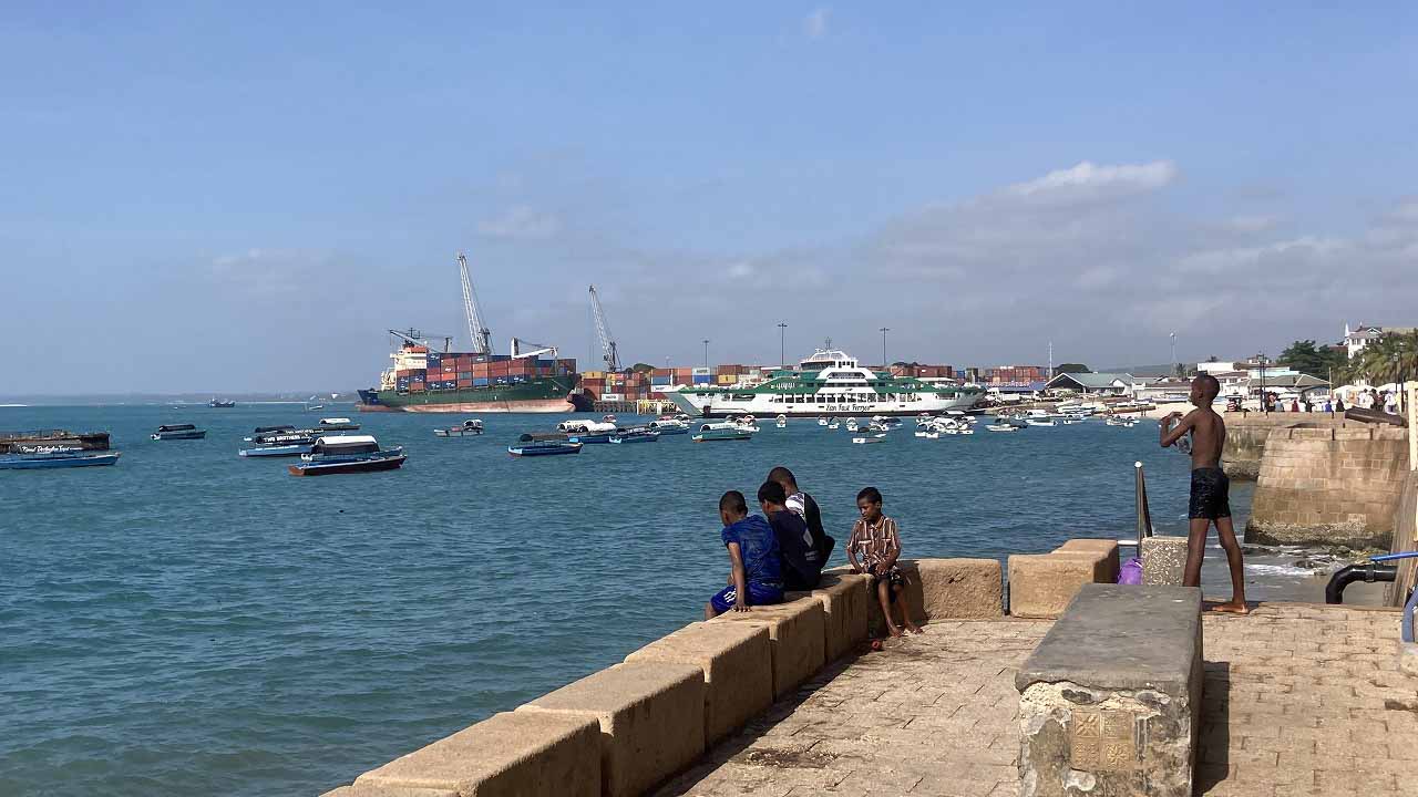 Local children sitting along the Stone Town seawall overlooking the harbor and anchored boats.