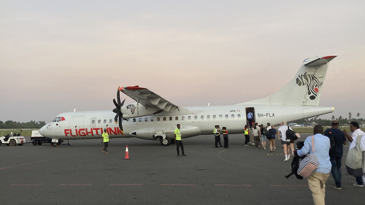 Passengers boarding a Flightlink turboprop aircraft on the runway at Zanzibar Airport.