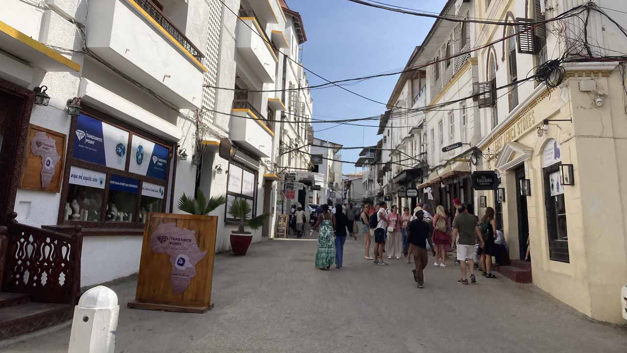 Busy pedestrian street in Stone Town lined with shops, historic buildings, and tourists.