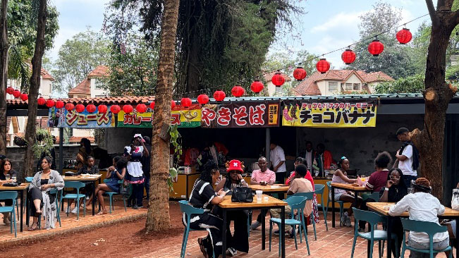 Outdoor dining area at a Japanese festival in Kenya, with food stalls, red lanterns, and visitors enjoying the event.