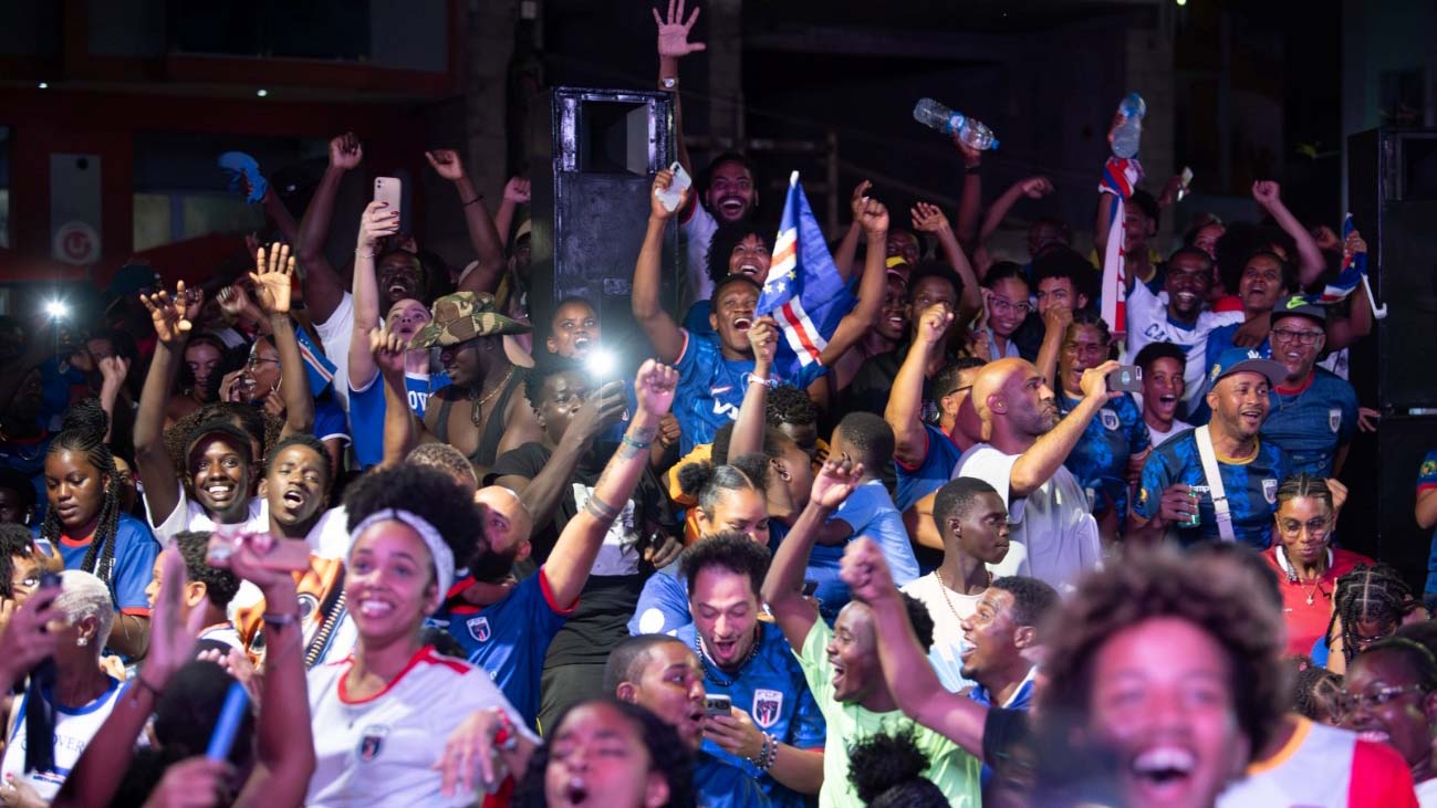 Cabo Verde football supporters celebrating together while waving national flags and wearing team shirts.