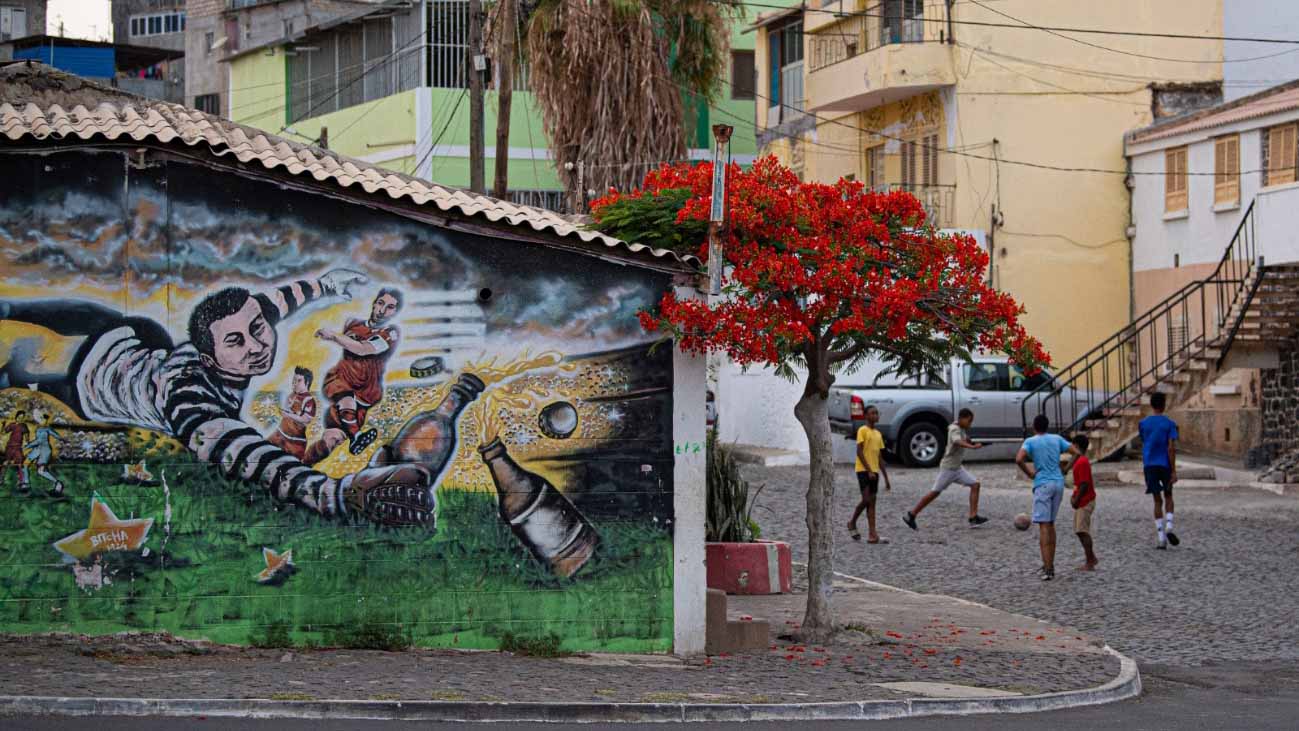 Children playing football beside colorful street art in a residential neighborhood in Cabo Verde.