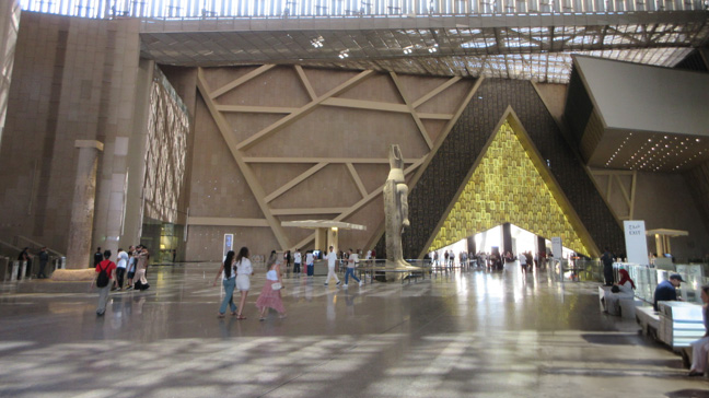 Grand entrance atrium of the Grand Egyptian Museum, featuring a monumental ancient Egyptian statue, striking geometric architecture, and a spacious interior filled with natural light.