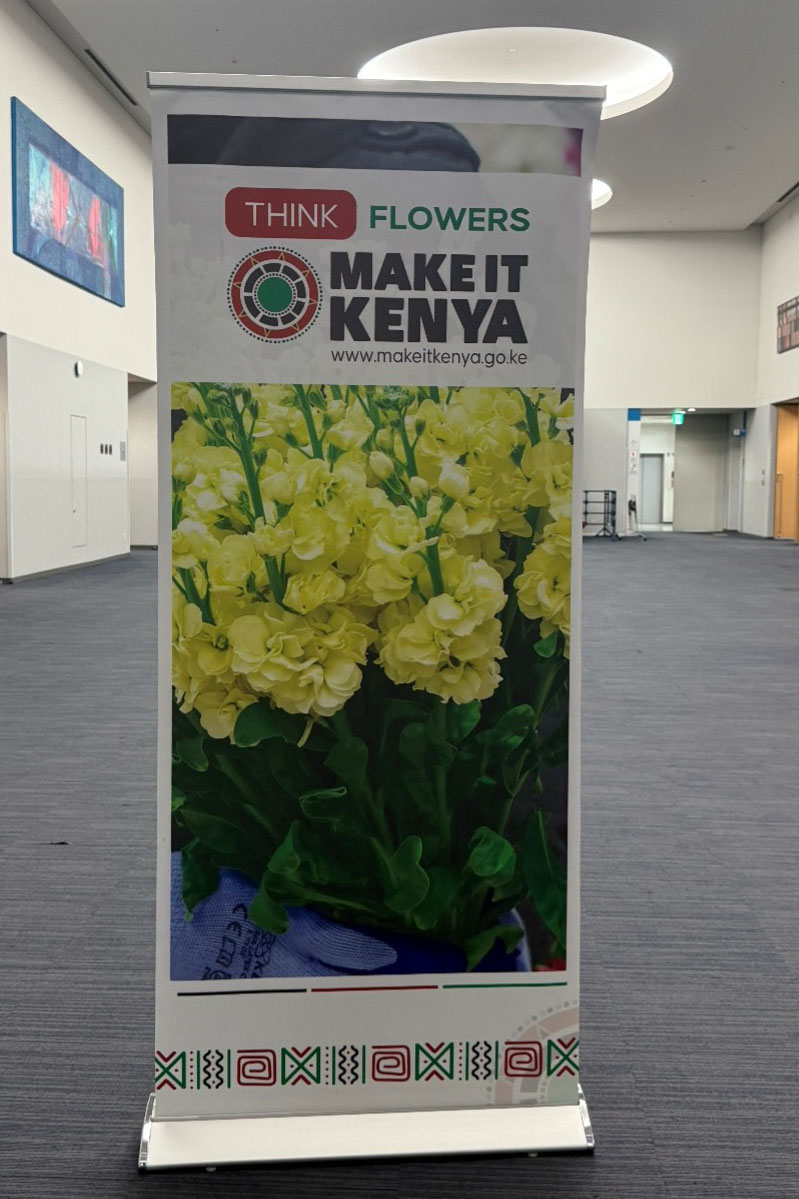 Promotional banner reading “THINK FLOWERS – MAKE IT KENYA” displayed in an EXPO2025 hallway, featuring yellow flowers and the official website.