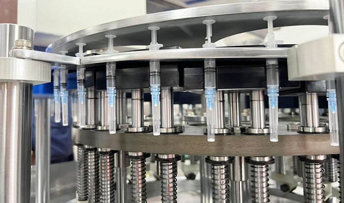 Close-up view of a high-precision industrial machine assembling or filling medical syringes in a production facility.